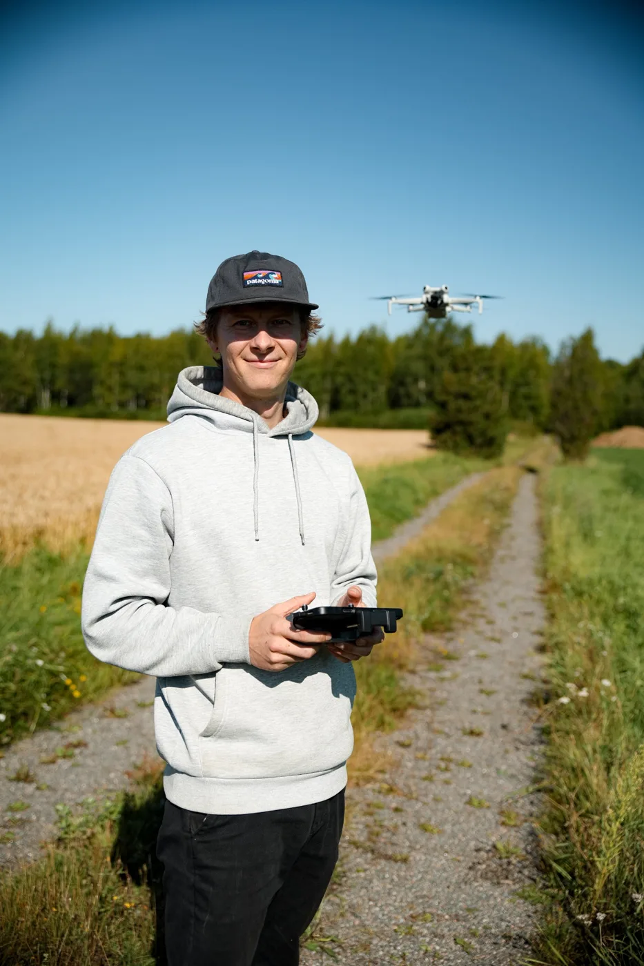 Valo Asuntokuvauksen kuvaaja ohjaamassa dronea peltotiellä